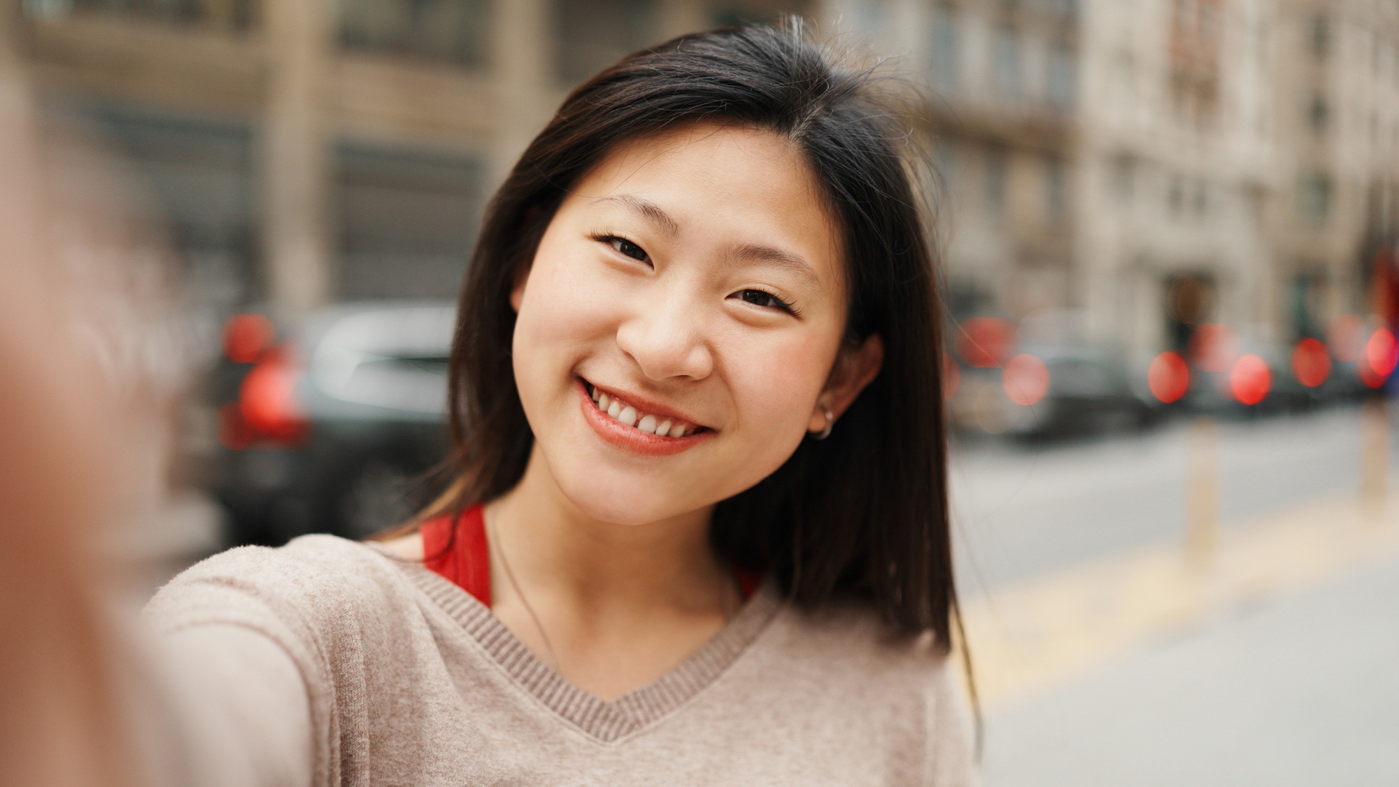 Asian girl taking selfie walking in the city. Long haired smiling woman making selfie on phone