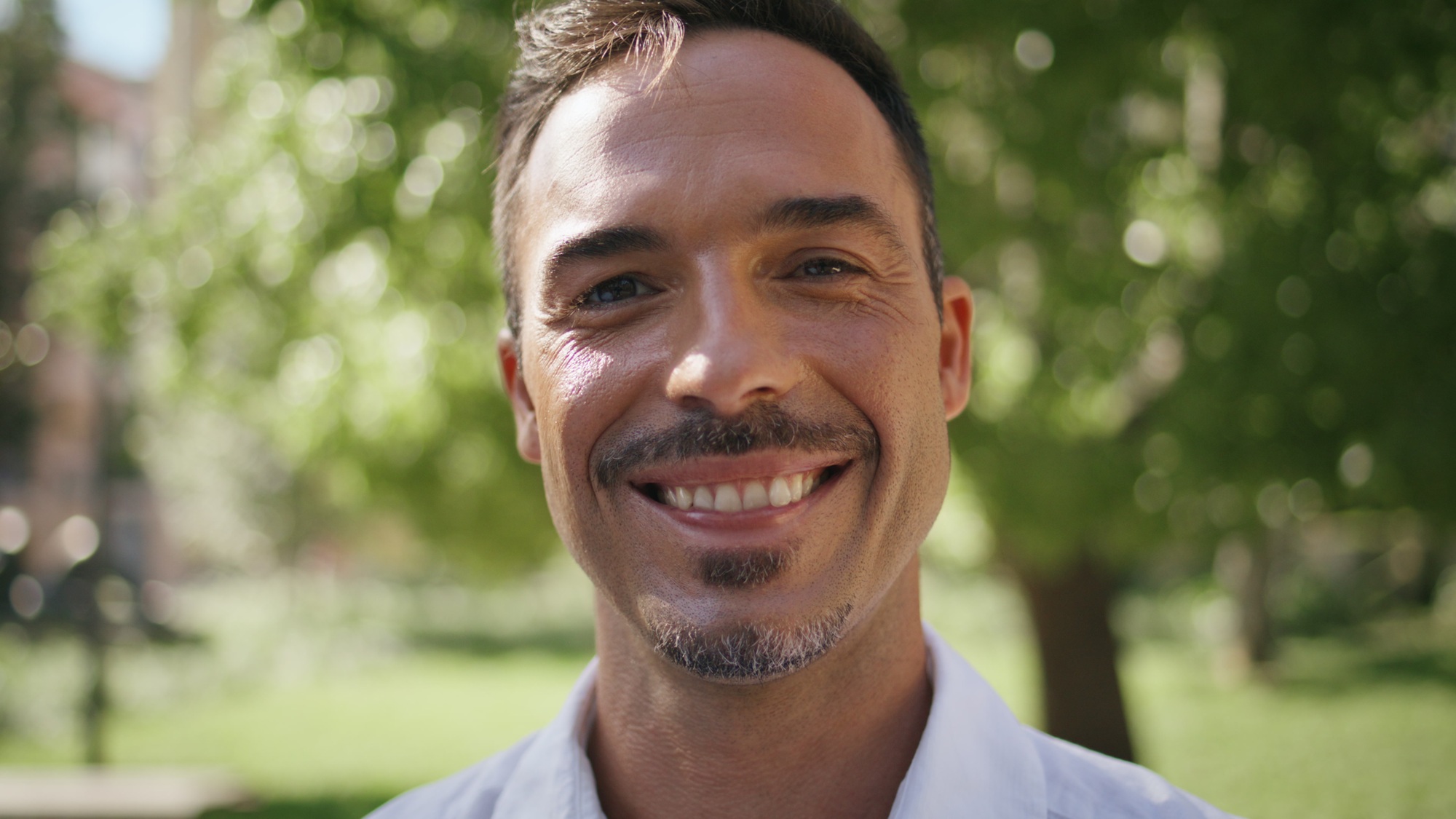 Portrait hispanic businessman smiling camera at green city. Man face posing
